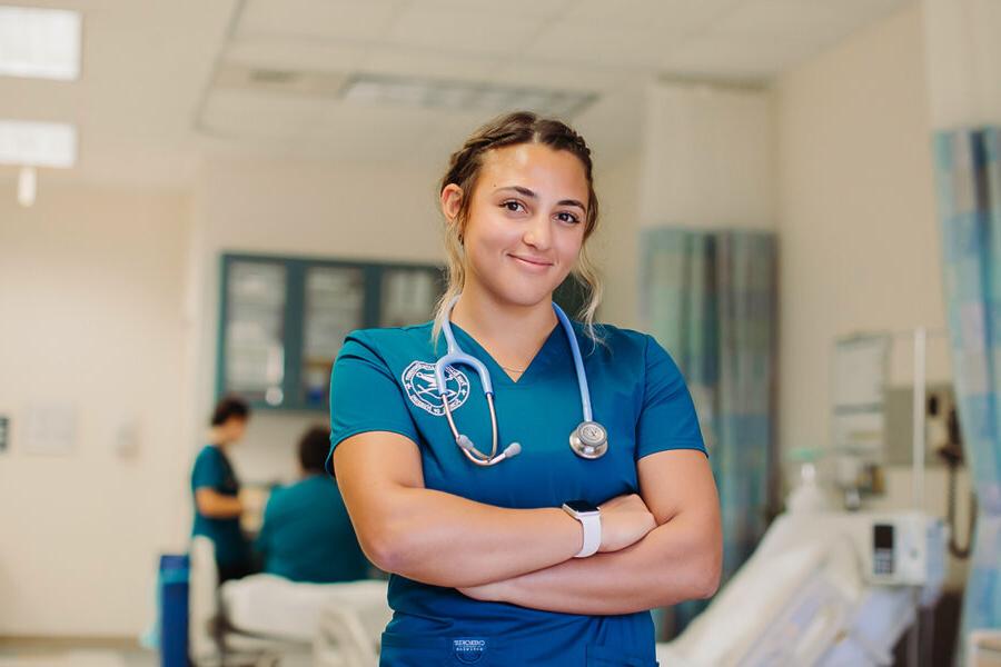 a nursing student wearing scrubs and a stethoscope smiling